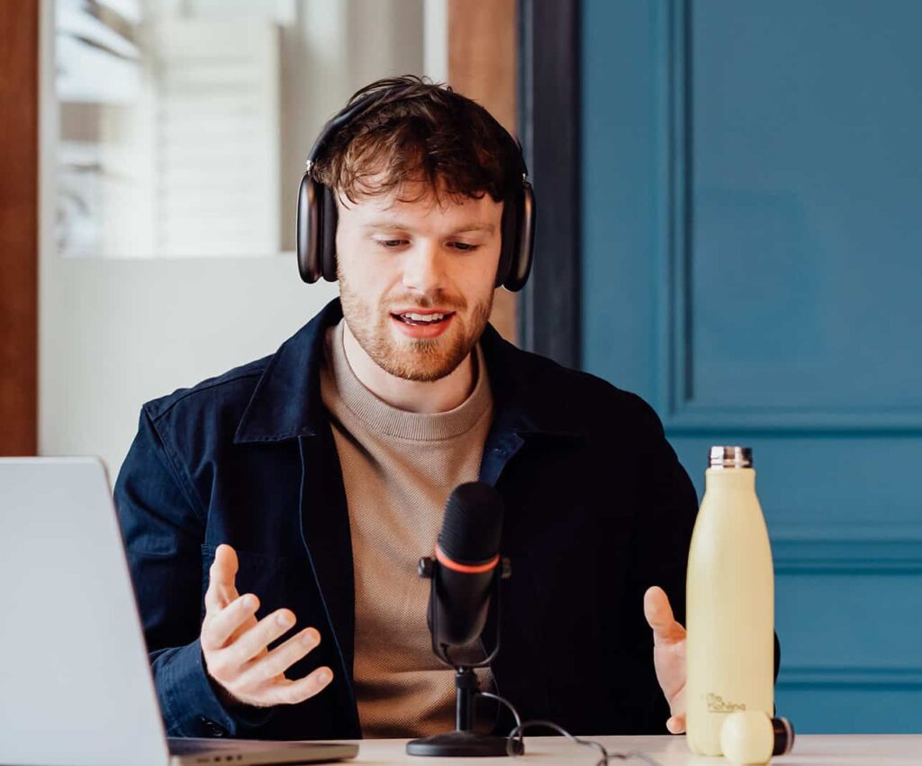 Callum Healey, AI lead at Agents of Change, speaking into a professional microphone and wearing headphones. He is explaining how to embed AI into a defined operating model to create leverage and maximise marketing agency performance.
