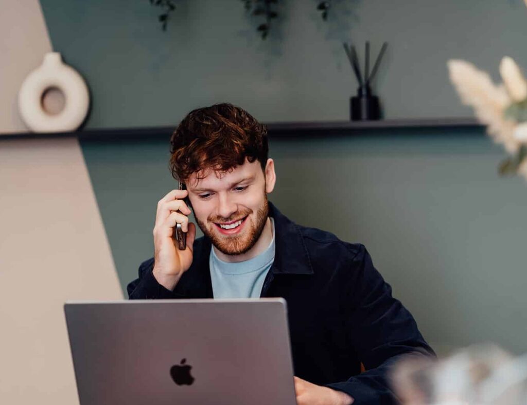 Callum Healey, AI lead at Agents of Change, smiling while on a discovery call. He is seated at a desk with an open laptop, representing the initial 30-minute structured conversation for marketing agencies looking to adopt AI.