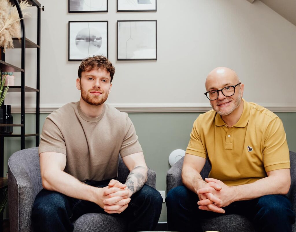 Hero image for Agents of Change featuring founders Gareth Healey (Agency Advisor, right) and Callum Healey (AI Lead, left). Gareth is wearing a yellow polo and glasses, while Callum is in a brown t-shirt. They are seated in grey armchairs, representing a consultancy focused on agency growth and AI adoption.